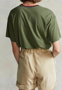 Olive green oversized t-shirt with a ribbed multicolor neckline, paired with beige shorts featuring folded cuffs and two back pockets.