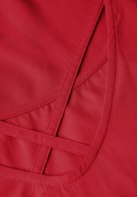 Tela roja con una textura suave presenta costuras decorativas entrecruzadas y detalles recortados, destacando un elemento de diseño geométrico.