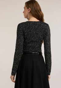 Czarny top z długim rękawem o błyszczącej fakturze, dopasowany fason. W zestawie z czarną spódnicą z wysokim stanem i błyszczącym paskiem.