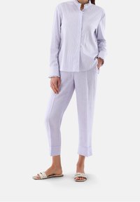 Camicia a righe viola chiaro con colletto alla cinese, abbinata a pantaloni tapered lilla chiaro e sandali a scivolo intrecciati color crema.