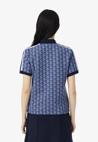 Polo shirt bleu à manches courtes avec un motif géométrique, col et poignets de couleur marine, et bandes latérales blanches.