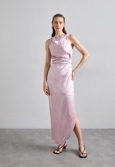 Lichtroze satin jurk met een mouwloos ontwerp, gedrapeerde taille en een zijsplit; gecombineerd met zwarte sleehakken. Gladde textuur.