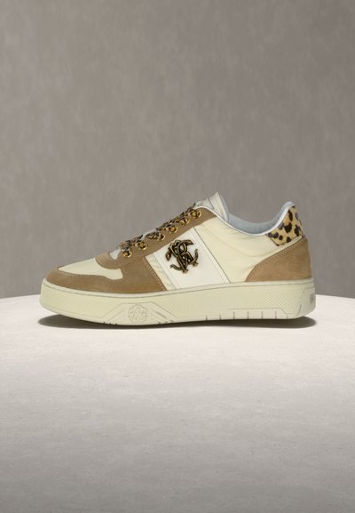 Μπεζ και κρεμ αθλητικό παπούτσι με καφέ σουέτ λεπτομέρειες, στοιχεία εκτύπωσης λεοπάρδαλης στη φτέρνα και τα κορδόνια, και χρυσό λογότυπο μονόγραμμα στο πλάι.