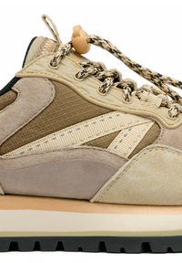 Zapatilla de ante en beige y marrón que presenta un cuerpo de malla texturizada, cordones con patrón y una suela acolchada con un acento en contraste.