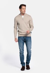 Beige gebreide pullover met een half-rits kraag, gecombineerd met blauwe jeans. Donkerbruine suède laarzen maken de outfit compleet, met een strakke pasvorm.