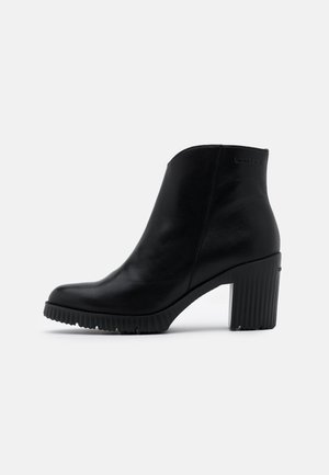 Černá kožená kotníková bota s kulatou špičkou, žebrovanou podrážkou a robustním vysokým podpatkem. Disponuje hladkým povrchem a minimálním brandingem.