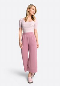 Gestreiftes Kurzarm-Oberteil in Hellrosa und Weiß, kombiniert mit lockeren, hochtaillierten, rosa Weitbein-Hosen. Vervollständigt mit hellrosa Clogs.