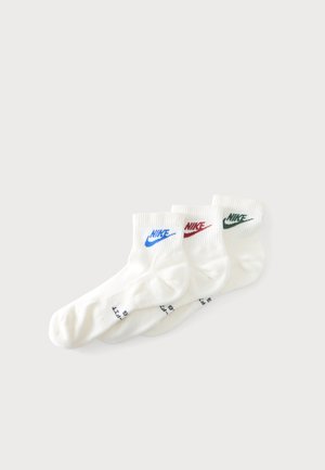Τρία ζεύγη λευκές κάλτσες αστραγάλου Nike με μπλε, κόκκινο και πράσινο λογότυπο στοιβαγμένα σε απλό λευκό φόντο.