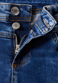 Siniset farkut, joissa on metallivetoketju hopeanvärillä, keltainen koristeommel ja kaksi nepparia vyötäröllä.