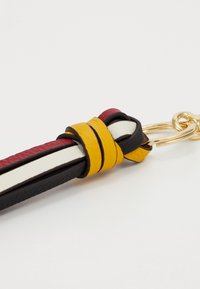 Porte-clés en cuir avec des bandes torsadées en bordeaux, noir et crème, maintenues par une finition jaune. Quincaillerie dorée et texture lisse.