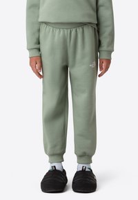 Light green sweatpants with an elastic waistband, ribbed cuffs, and a small white logo printed on the thigh. Smooth texture, relaxed fit.