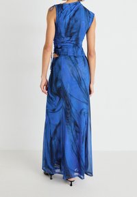 Niebieska sukienka z wzorem wiru, dopasowaną górą i asymetrycznym krojem na ramionach. Materiał wydaje się lekki i zwiewny, z rozcięciem i bocznymi wiązaniami.