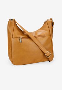 Bolso de hombro de cuero tono marrón claro con forma redondeada, bolsillo frontal con cremallera, correa ajustable y textura suave. Detalles en tono dorado.