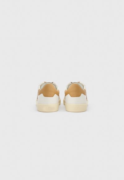 Ζευγάρι λευκών αθλητικών παπουτσιών με μπεζ πατήματα στη φτέρνα, που φαίνονται από πίσω, σε απλό ανοιχτό γκρι φόντο.