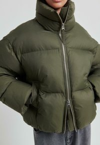 Puffig olivgrön jacka med hög krage, dragkedja i fram och sidofickor. Tillverkad av slät, isolerande tyg med kviltat mönster.