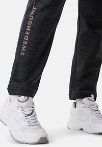 Mörkgrå träningsbyxor med "SWEDEMOUNT" i ljusrosa bokstäver; matchade med klumpiga vita sneakers med gråa accenter och snörning.