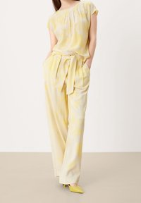 Light yellow floral blouse with pleats paired with wide-leg yellow pants. Both made of smooth fabric; pants feature a tied waistband.