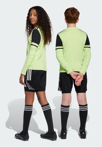 Ungdomsfotbollsoutfit som består av en neongrön långärmad tröja med svarta detaljer, svarta shorts och randiga knähöga strumpor.