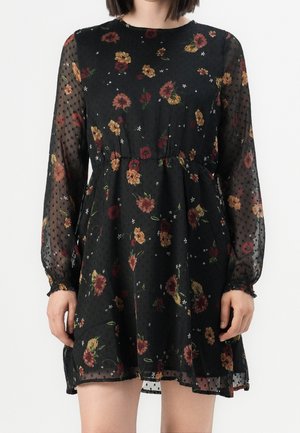 Vestido largo negro de manga larga transparente con estampado floral rojo y amarillo, cintura fruncida y textura de puntos en las mangas y la tela.