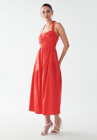 Punane puuvillane kaelarätiga kleit, millel on kehasse vormitud ülaosa, volangidetailid ja kihiline seelik. Kandmiseks valgete kontsakingade ja kõrvarõngastega.