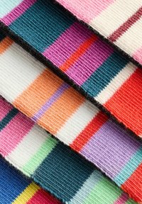 Kankaita värikkäitä kangaskudoksia, joissa on raitoja vaaleanpunaisessa, tealissä, oranssissa, purppurassa ja valkoisessa, ja joissa on teksturoitu pinta ja vaihtelevat leveydet.