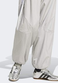 Ljusgrå, löst sittande byxor med stora sidofickor, tillsammans med blanka silverfärgade sportskor med svarta ränder och en texturerad yta.