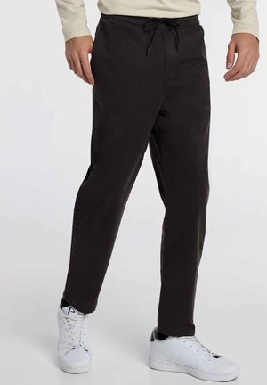 Pantalon noir en coton avec taille élastique et poches latérales, doté d'une coupe droite et d'un tissu léger. Associé à des baskets blanches.