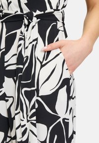 Zwart-wit gedrukt jumpsuit met een knoopdetail bij de taille, voorzien van een zijzak en een bloemenpatroon op zachte stof.