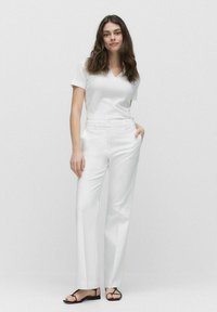 Witte v-hals top met textuur, gecombineerd met op maat gemaakte witte broeken met zijzakken en een rechte pijpdesign. Zwarte sandaaltjes met bandjes.