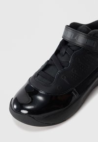 Baskets de sport noires avec embout brillant, tige en maille et cuir, fermeture à lacets à l'avant et sangle de cheville avec logo et imprimé à motifs.