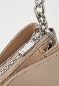 Sac à main beige en similicuir texturé, avec quincaillerie argentée et fermeture éclair. Doté d'une poignée en chaîne métallique épaisse. Design minimaliste.
