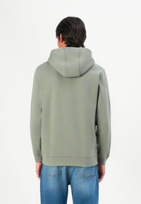 Sudadera con capucha en verde claro, de textura suave, corte relajado y puños y dobladillo acanalados; combinada con jeans azules.