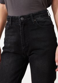 Vaqueros negros de denim de talle alto con cierre de botones, bolsillos delanteros y una textura suave, con un desvanecimiento sutil en los muslos.