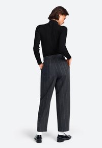 Schwarzer gerippter Rollkragenpullover, figurbetontes Design. Graue gestreifte Hochbundhose mit seitlichen Taschen und lockerer Passform. Schwarze Schuhe mit weißen Socken.