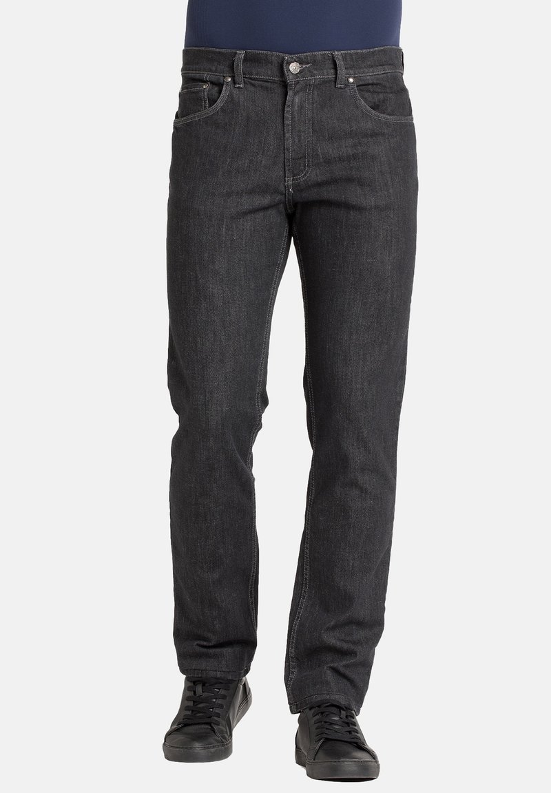 Zwarte spijkerbroek van denim met rechte pijpen, vijf zakken en subtiele stiksel details. Draagt zwarte sneakers en een marineblauwe top.