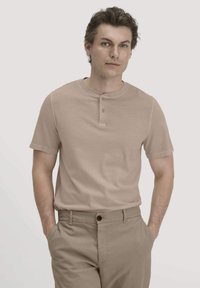 Beige Kurzarm-Henley-Shirt mit einer Knopfleiste mit drei Knöpfen und einer weichen, glatten Textur, kombiniert mit hellen, sandfarbenen Hosen.