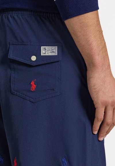 Jūriniai šortai su elastiška juosmeniu, turintys kišenę su mygtuku, išsiuvinėtus raudonus ir mėlynus polo logotipus bei audinio etiketę.