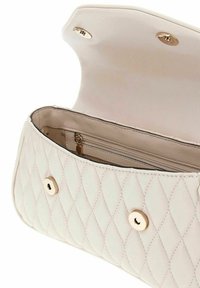Borsa trapuntata beige aperta per mostrare la tasca interna con zip e le chiusure a bottone magnetico dorate sulla patta e sul corpo della borsa.