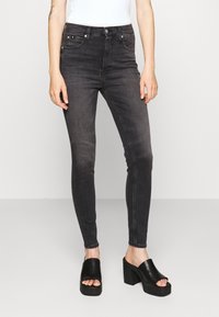 Pantalones vaqueros negros ajustados con un acabado deslavado, con una cintura de altura media, cinco bolsillos y un cierre de botón. Combinados con sandalias de plataforma negras y gruesas.