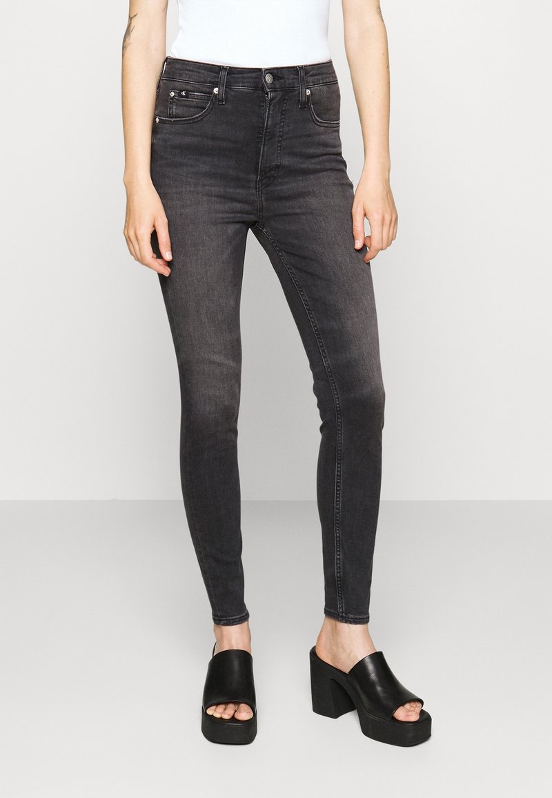 Pantalones vaqueros negros ajustados con un acabado deslavado, con una cintura de altura media, cinco bolsillos y un cierre de botón. Combinados con sandalias de plataforma negras y gruesas.