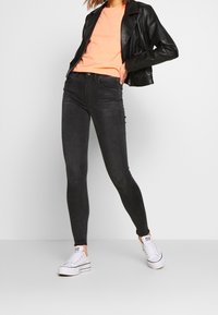 Svarta tajta jeans med hög midja, gjorda av stretchdenim. Matchas med en orange T-shirt och en svart läderjacka, kompletterat med vita sneakers.