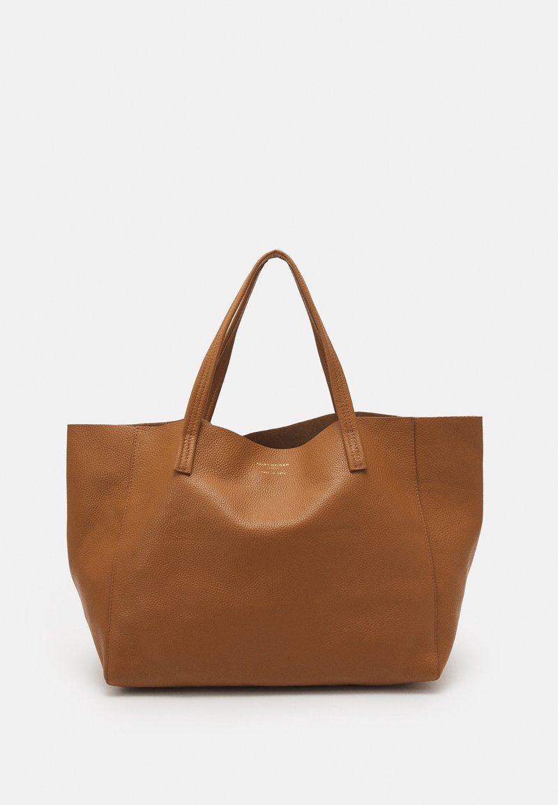 Hnědá kožená taška přes rameno s texturovaným povrchem, širokým otevřeným horním dílem a dvěma pevnými uchy. Vyznačuje se minimalistickým designem bez viditelného kovového vybavení.