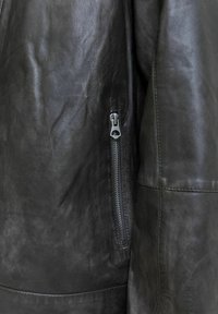 Chaqueta de cuero negro con una textura suave, cremallera prominente en el lado izquierdo y costuras entalladas para un diseño ajustado.