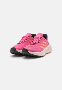 Zapatillas deportivas rosas con parte superior transpirable, tres franjas naranjas, suela texturizada con tracción negra y entresuela moteada.