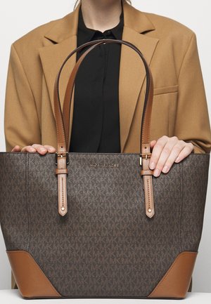 Sac cabas marron avec un motif texturé, des accents en cuir beige, deux poignées et un logo. Le sac a un design structuré et est spacieux.