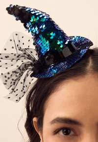 Blauw-zwart pailletten heksenhoed met een puntige top, een zwarte satijnen band en zwarte tule met stippen als accenten. Glanzend en textuurrijk oppervlak.