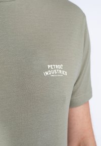 Polo de manga corta en color verde oliva con una tela texturizada y un logo bordado en blanco: "PETROL INDUSTRIES" en el lado izquierdo del pecho.
