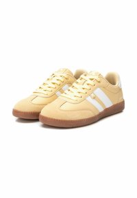 Zapatillas deportivas amarillas con parte superior de ante y sintético, que presentan rayas blancas, suela de goma texturizada y cordones planos. Diseño centrado en la comodidad.
