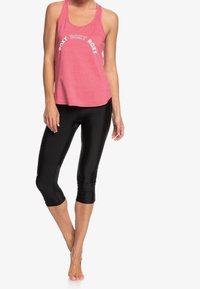 Top senza maniche di colore rosa con la scritta "ROXY" stampata in bianco, abbinato a leggings capri neri, caratterizzati da una texture di tessuto liscia e lucida.
