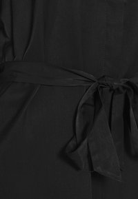 Abito in tessuto nero con una fascia annodata in vita, che presenta una texture morbida e una finitura liscia e leggermente lucida.